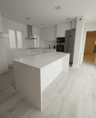 Imagen de una cocina reformada por MAM Experience Building, destacando una isla central amplia, diseño contemporáneo en blanco, electrodomésticos de acero inoxidable y acabados que aportan luminosidad y elegancia al espacio.
