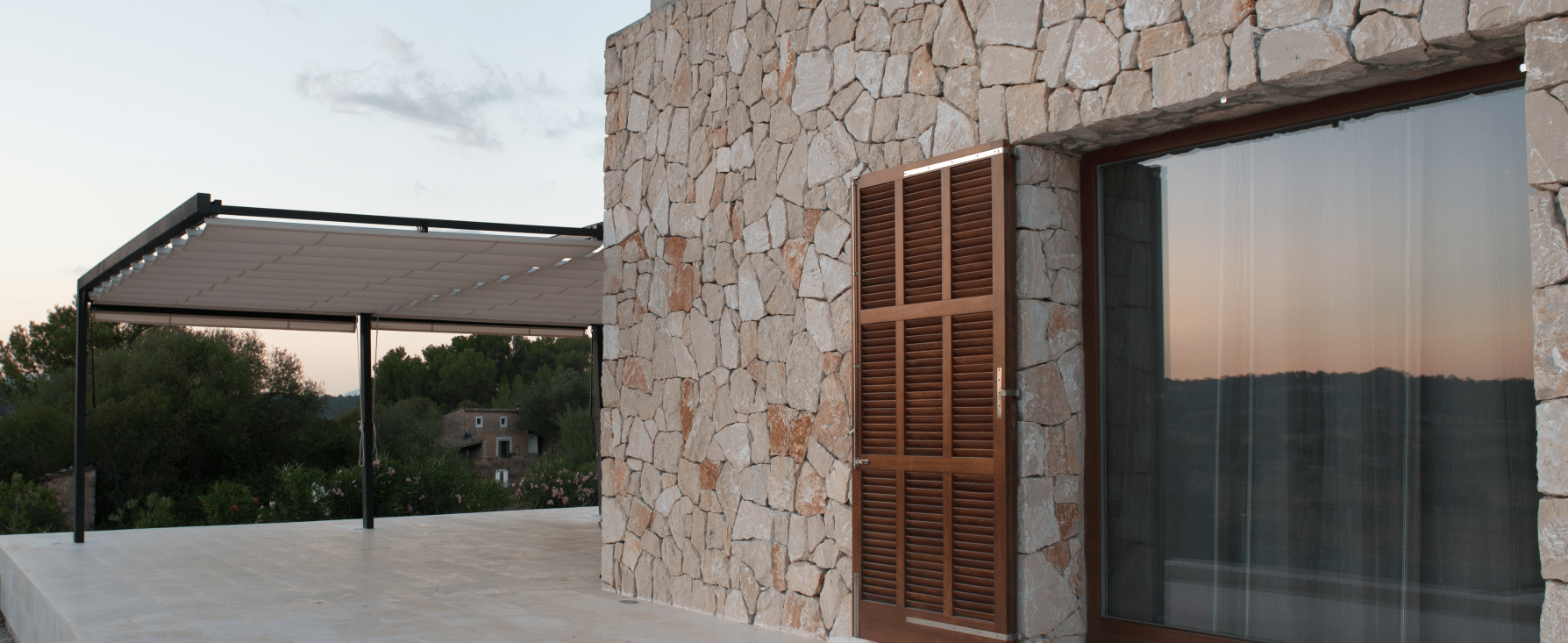 Imagen de una terraza con pérgola en una vivienda de piedra, diseñada por MAM Experience Building, mostrando detalles arquitectónicos rústicos y modernos con vistas a un entorno natural.