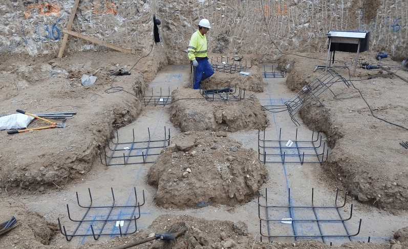 Imagen del proceso de construcción de cimientos realizado por MAM Experience Building, mostrando un trabajador en el sitio con las estructuras de acero preparadas para ser integradas en los cimientos de la edificación.